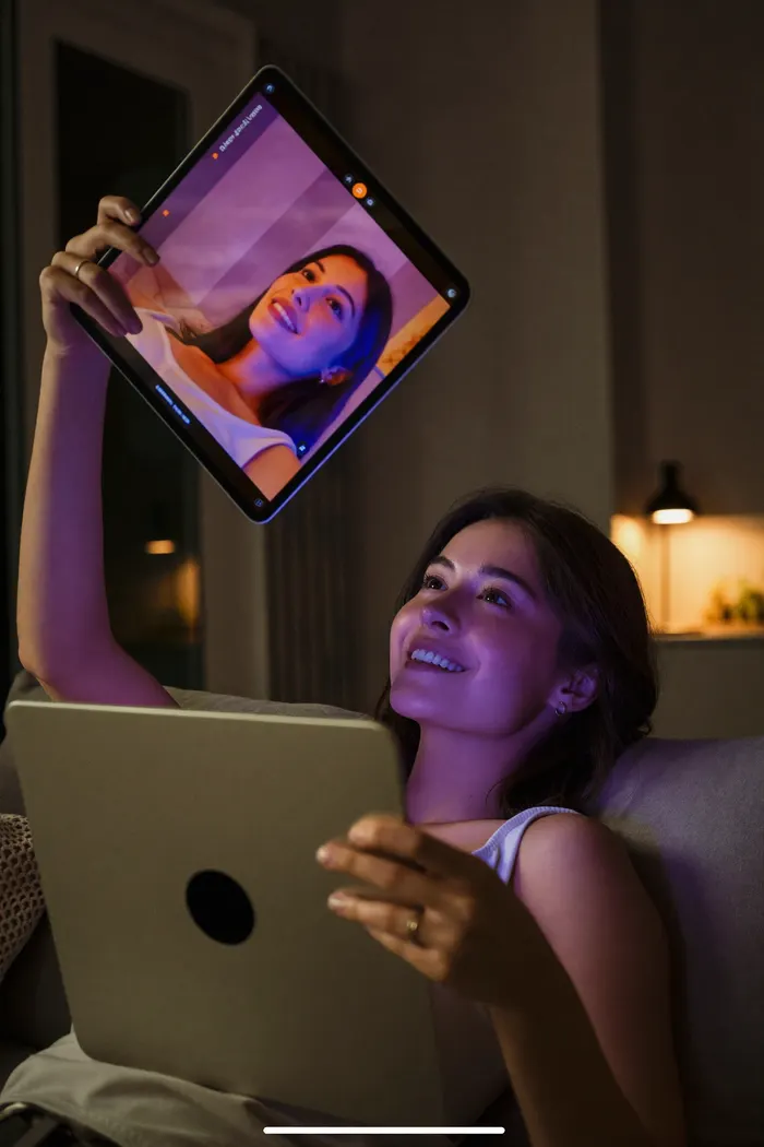 Woman on a couch smiling at a live cam stream on her tablet